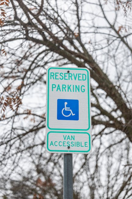 A rectangular white sign with bold black text reading 'NO PARKING DAY OR NIGHT' is mounted on a grey wooden door or wall. The sign is secured with four silver screws, one in each corner. The background surface has visible horizontal and vertical paneling, typical of an exterior dwelling or property entrance. The lighting is neutral, with no shadows or reflections, indicating natural or soft indoor light. This sign, displayed outside a property, is related to parking regulations in relation to house removals or moving services, such as those offered by Kensington Removals, highlighting restrictions during logistical moving operations and adherence to local permit rules for furniture transport or home relocation within the Kensington area.